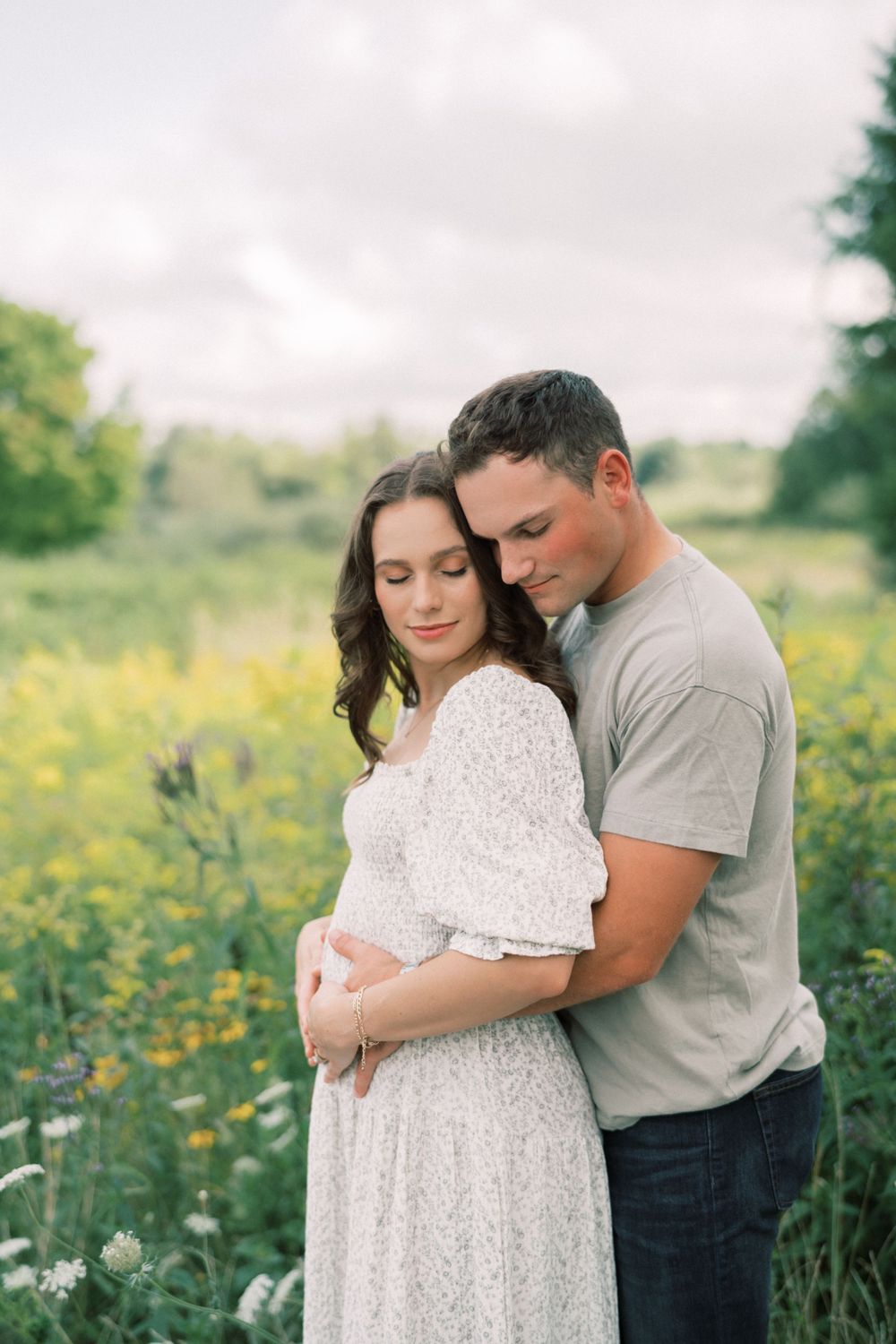 Intimate embrace between couple in flowering meadow during pregnancy photoshoot.