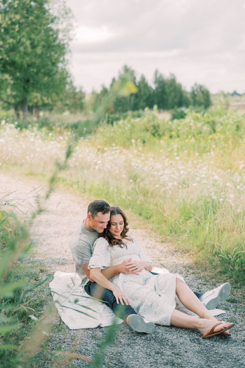 Couple relaxes on blanket along wildflower-lined path during maternity session.