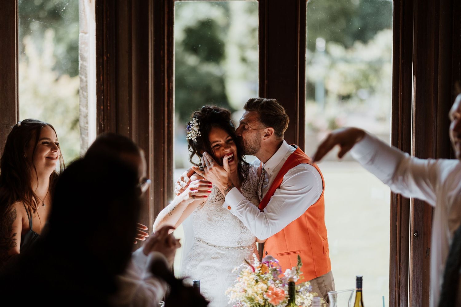 Joyful couple sharing intimate moment during wedding celebration with guests and floral decor.