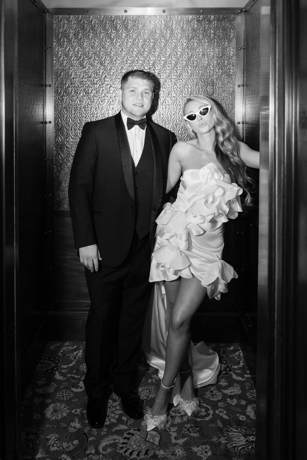 Black and white elevator portrait with vintage wallpaper backdrop and formal attire.