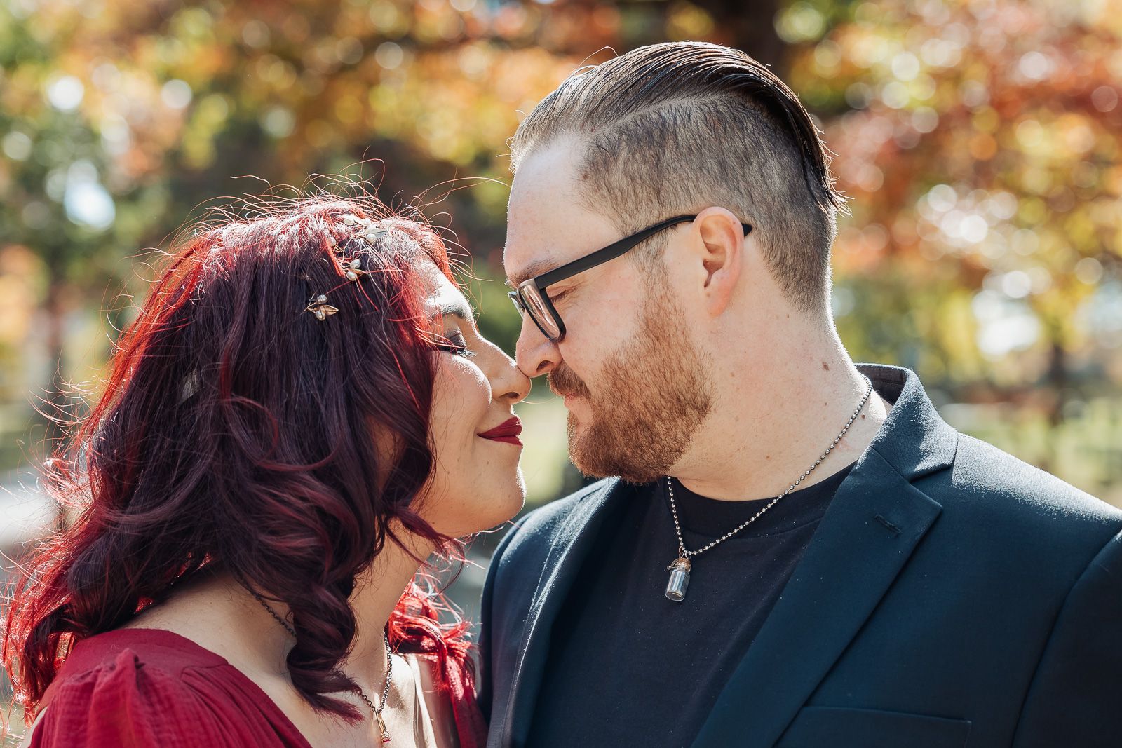 An intimate close-up portrait of a couple sharing a tender moment amid autumn trees.