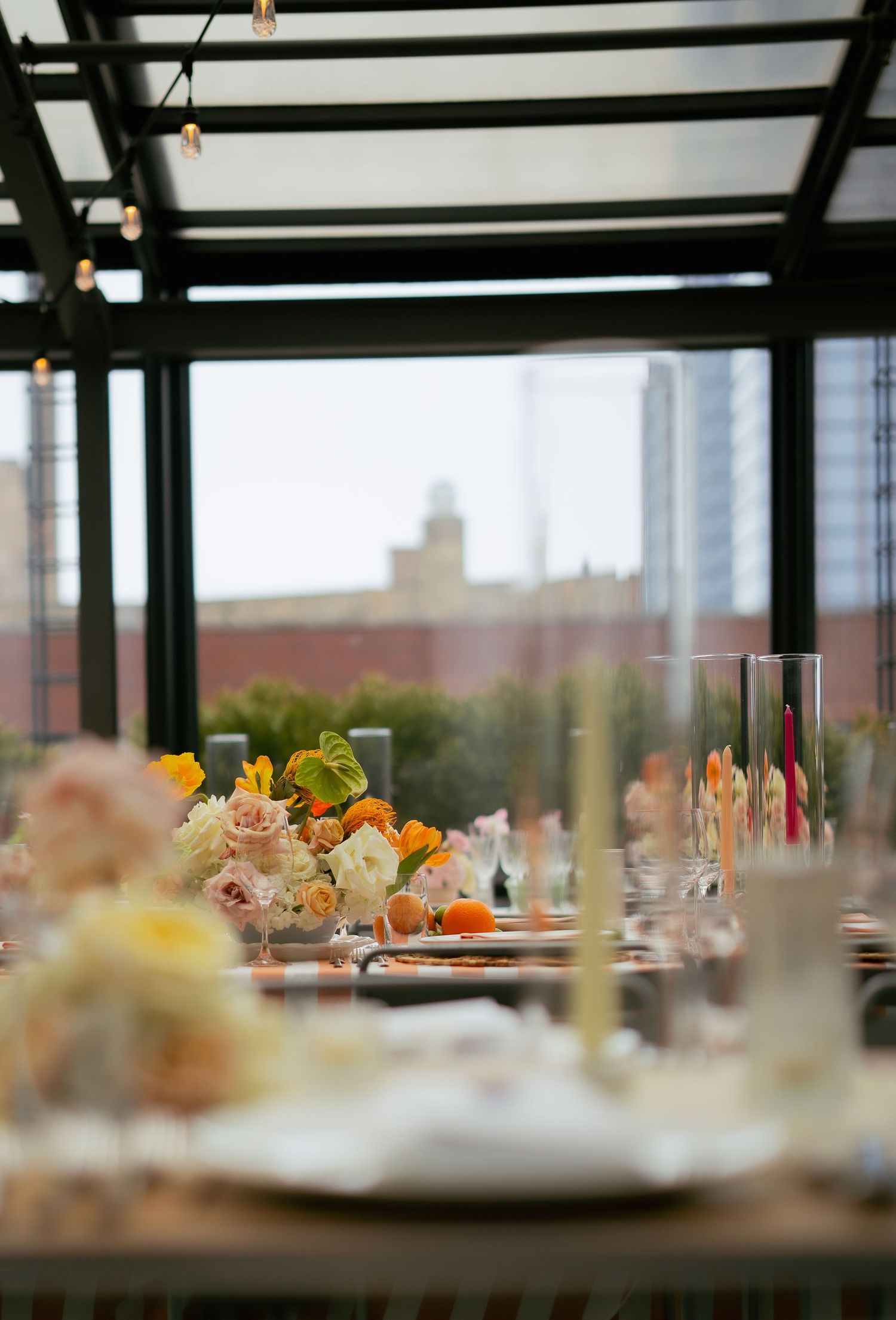 Elegant table setting with floral centerpieces and city skyline view through glass ceiling.