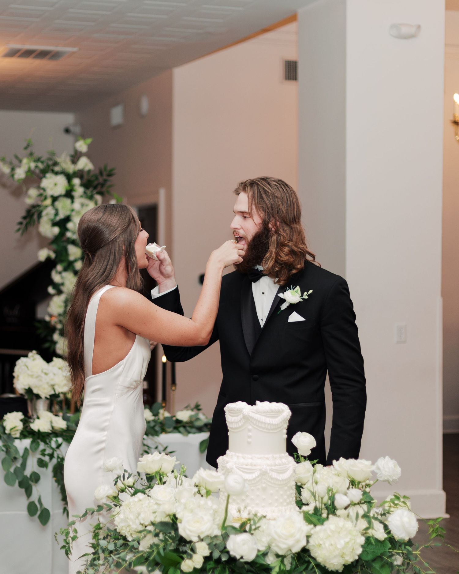 Couple sharing a playful moment while cutting their white wedding cake surrounded by floral decorations.