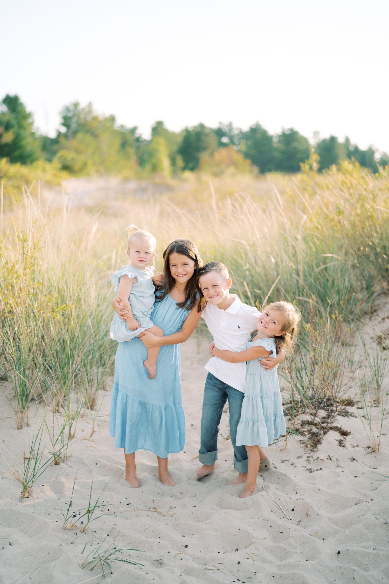 Family portrait on sandy beach with tall grass and natural lighting.