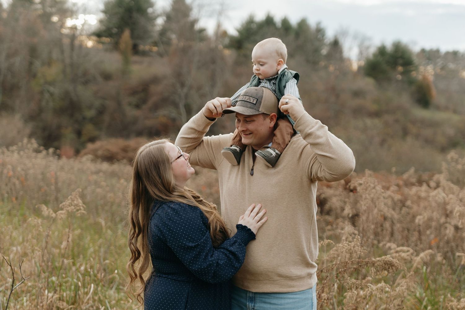 Family of three enjoying playful moment together in autumn field.