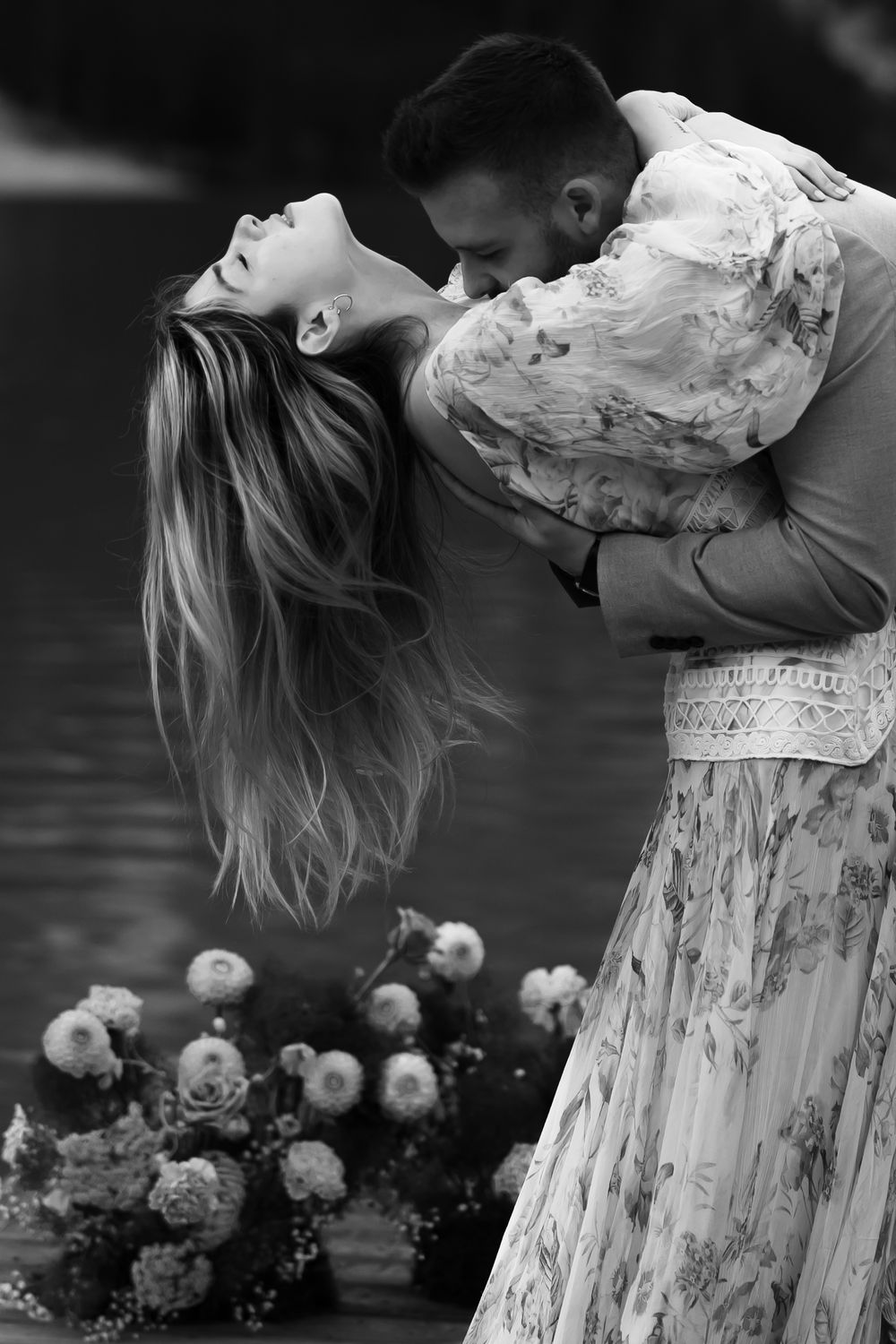 A romantic black and white photograph of a couple embracing in formal wear with roses in the foreground.