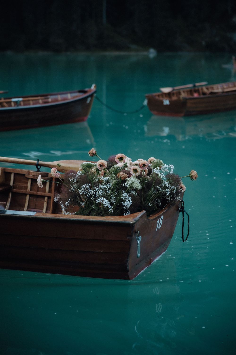 Wooden boats float on turquoise waters with white flowers decorating one of the vessels.
