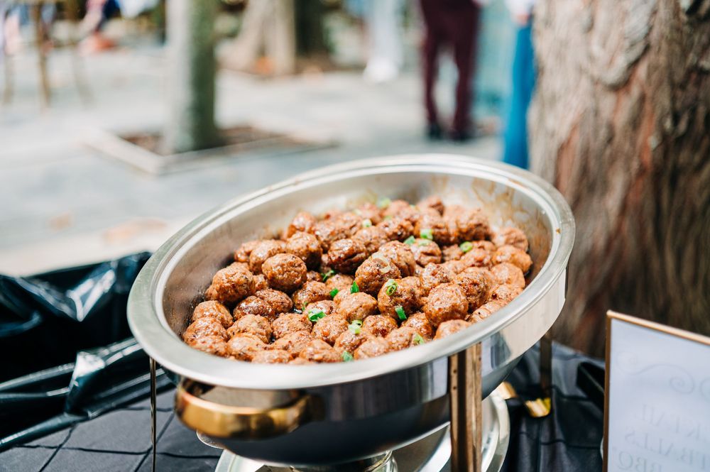 A stainless steel chafing dish filled with crispy fried chicken pieces at a catered outdoor event.
