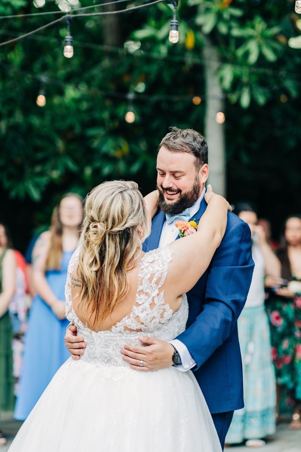 Couple sharing an intimate dance moment at an outdoor wedding reception with string lights and greenery.