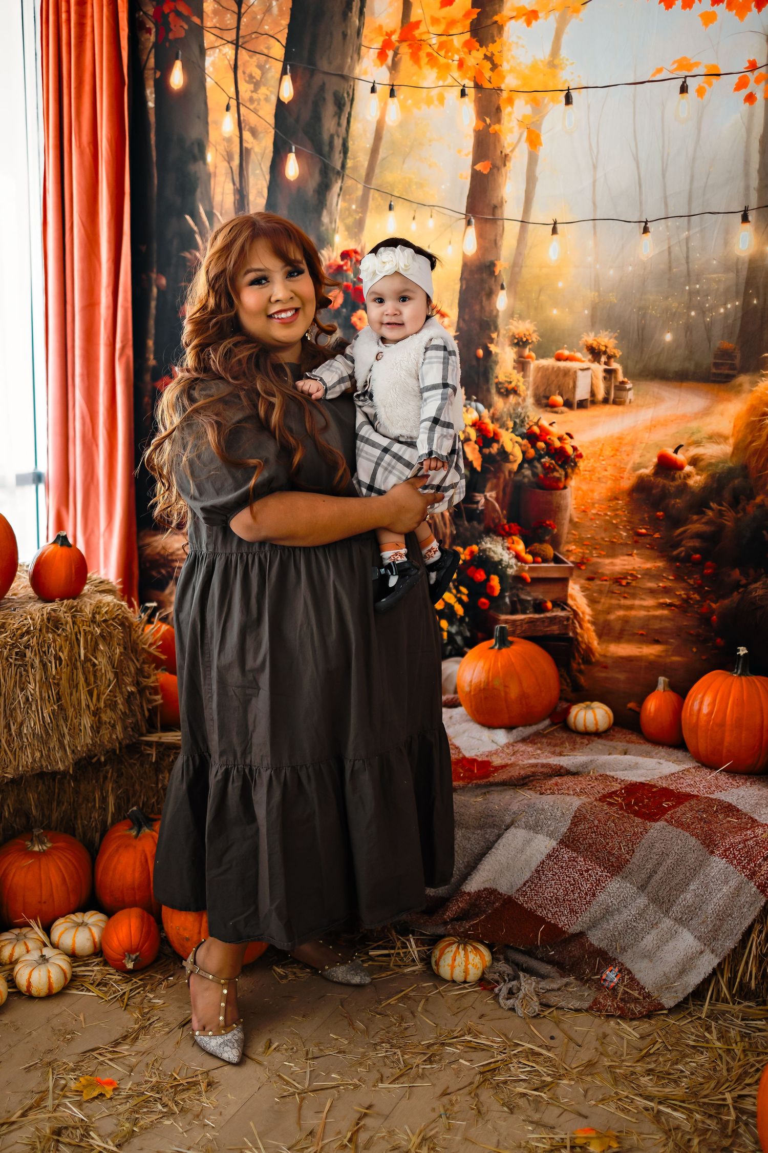 Cozy fall photo setup with hay bales, string lights, plaid blankets, orange pumpkins and autumn decor against a studio backdrop.