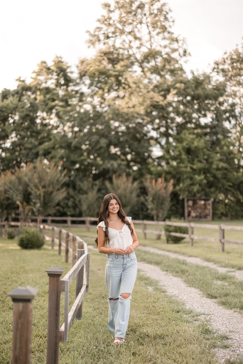 A person walks along a gravel pathway beside a wooden fence on a rural farm property during golden hour.