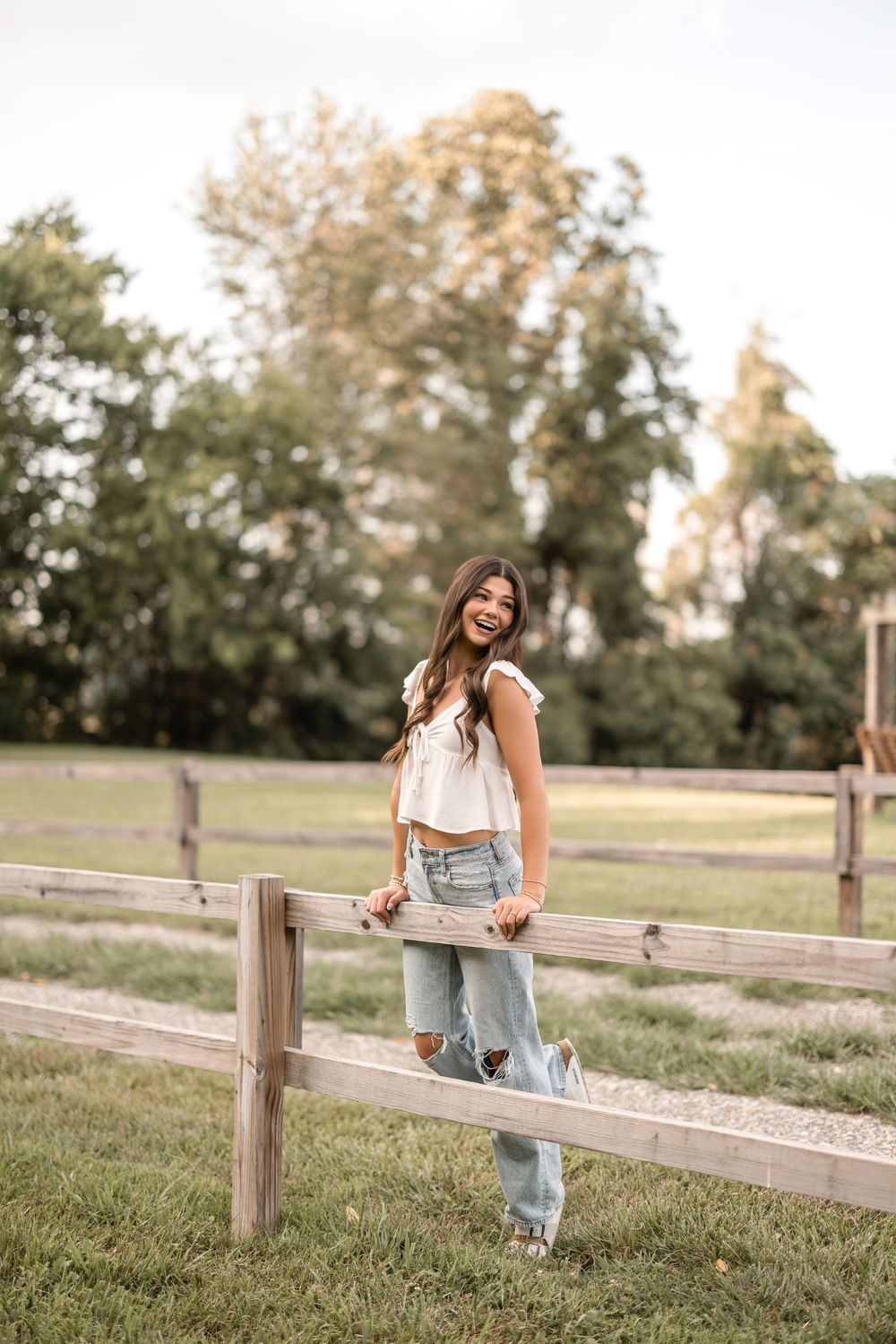Casual summer style photo of distressed jeans and white crop top in rustic country setting with wooden fence.
