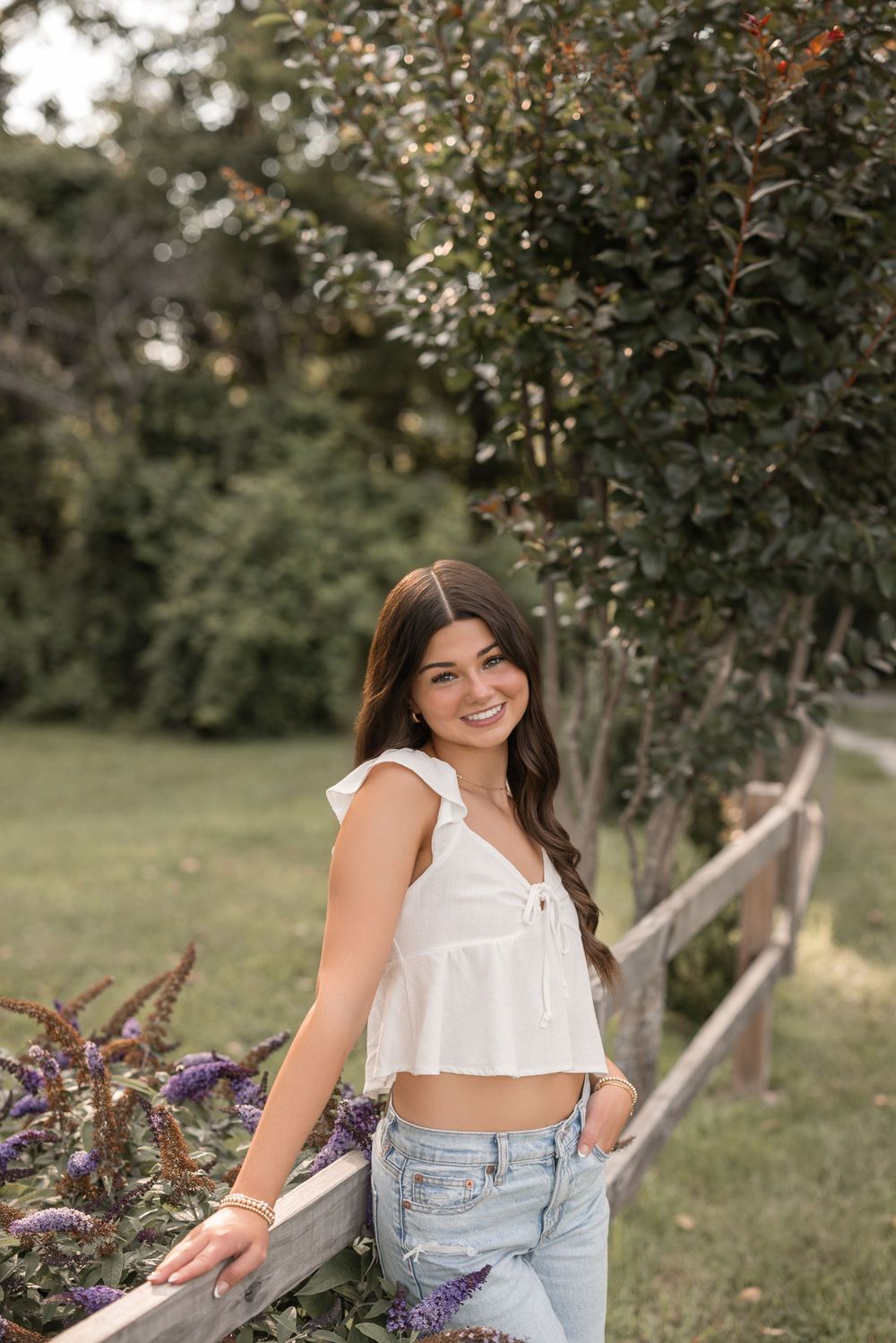 A white summer top and denim outfit styled casually in an outdoor garden setting with rustic wooden fencing.