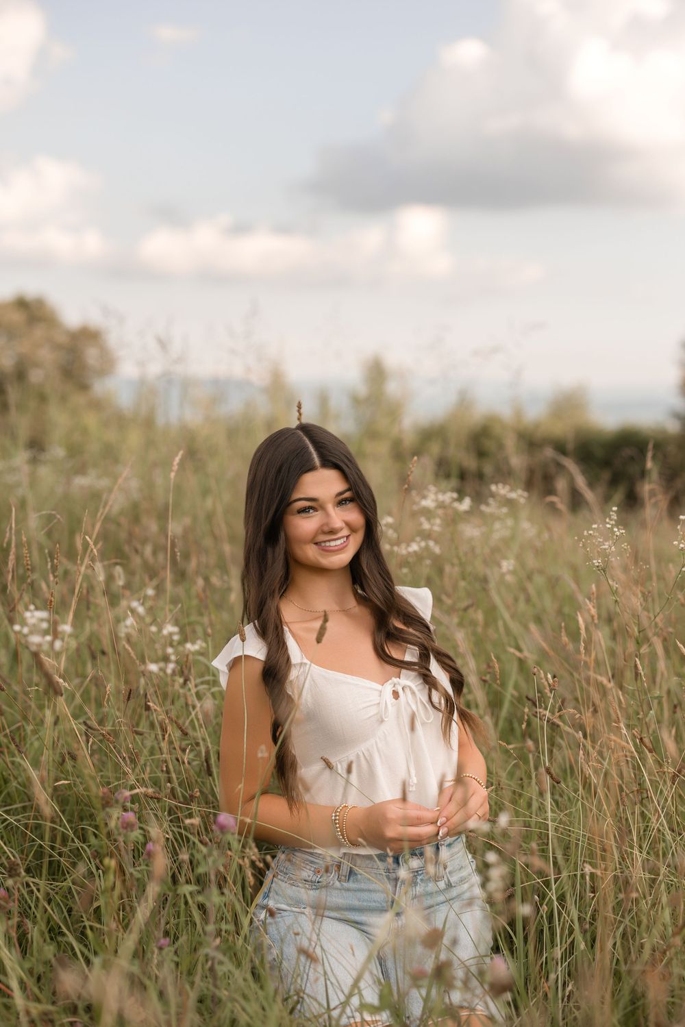 Someone wearing a white top and jeans poses in a sunny wildflower meadow on a summer afternoon.