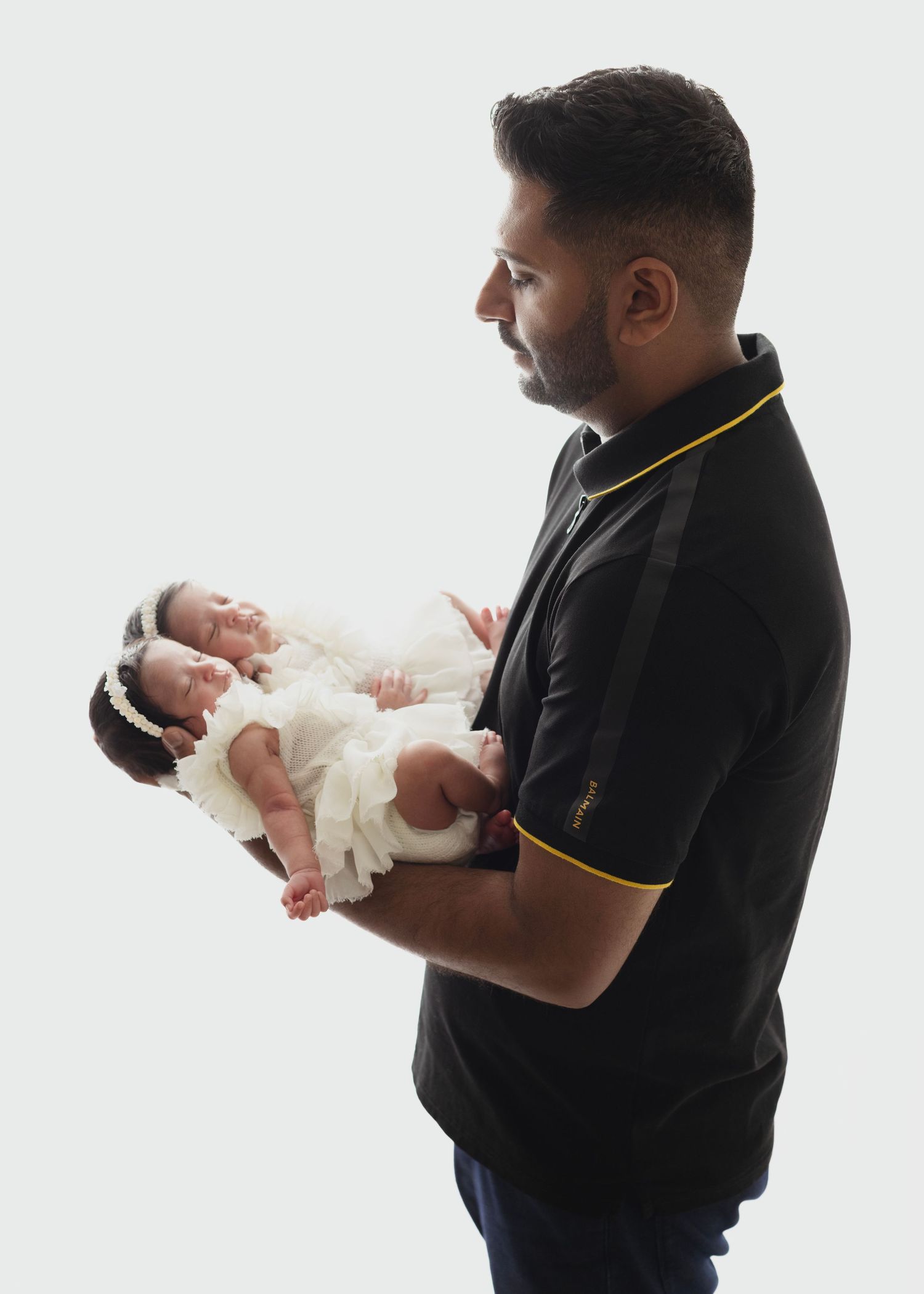 Elizabeth Lang Photography newborn photos dad hold newborn twin girls in a bright backlit photo with little white dresses.