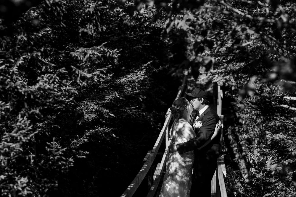 A figure stands in dramatic black and white lighting against a shadowy background with trees and foliage.
