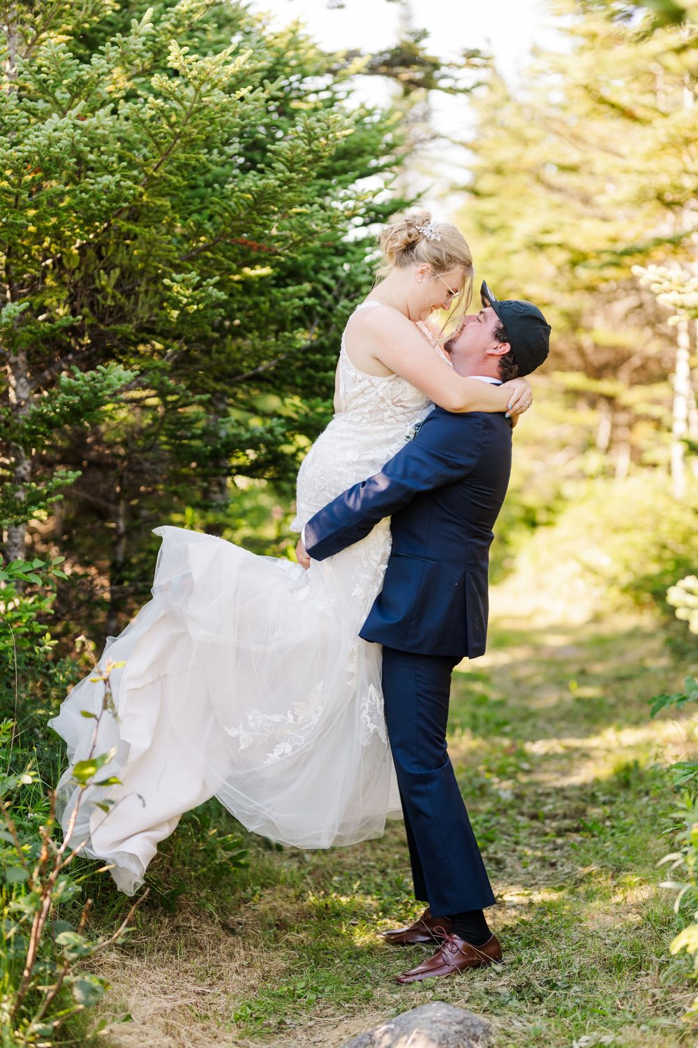A couple in wedding attire dances and spins together outdoors surrounded by greenery in a romantic forest setting.