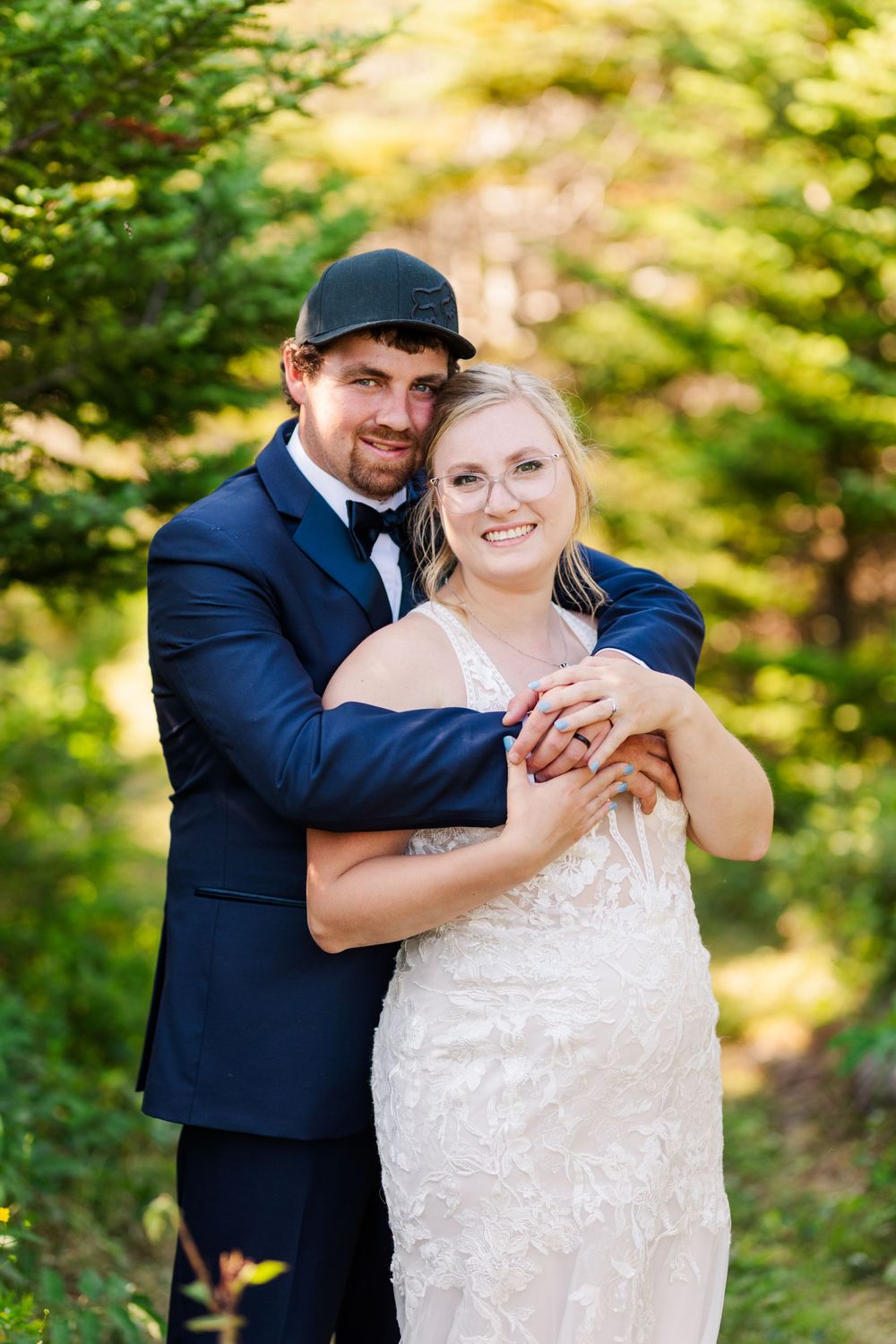 A couple embraces in an outdoor wedding photo with a natural green forest backdrop.