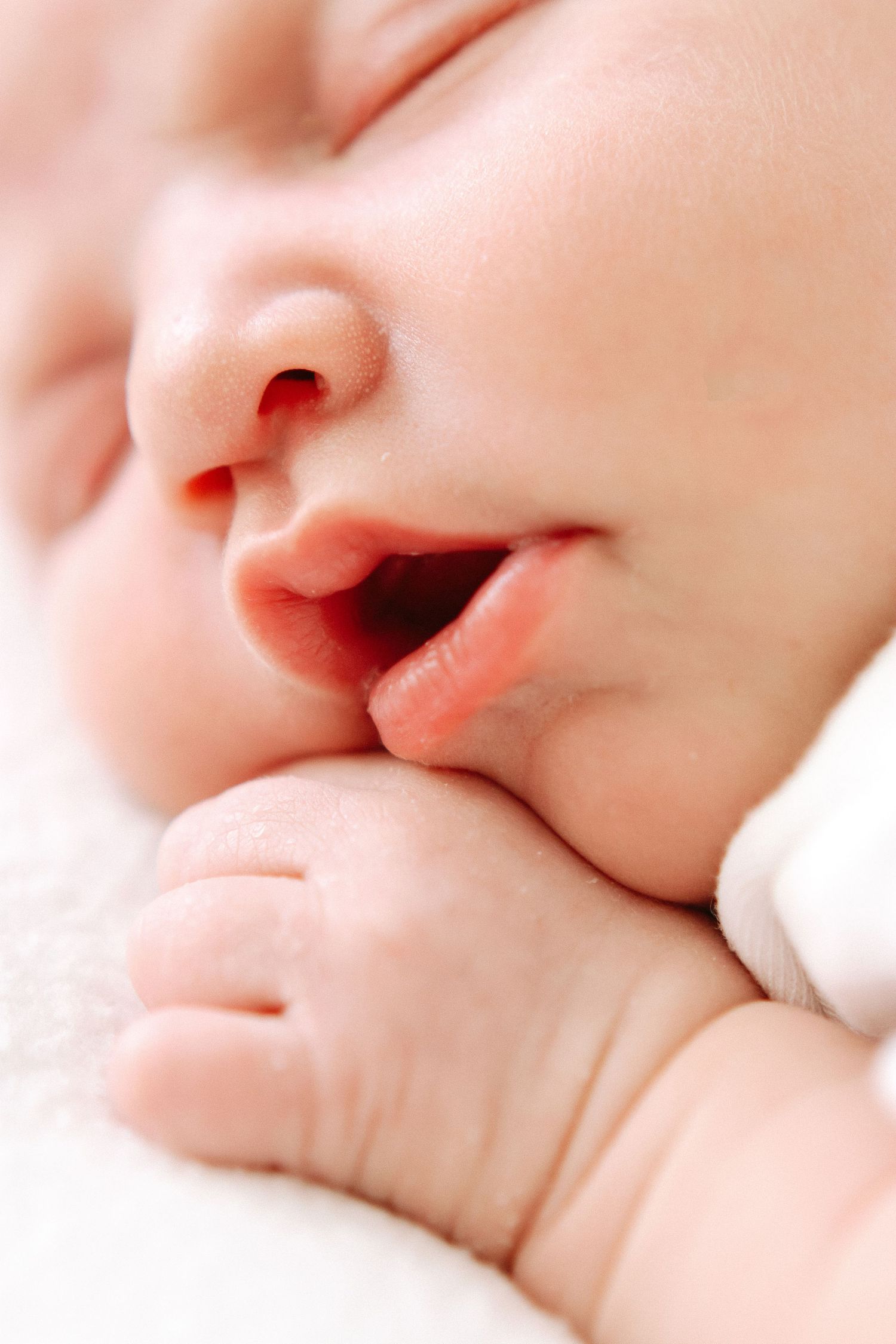 Closeup of a sleeping baby's face and tiny hand in soft pink lighting.