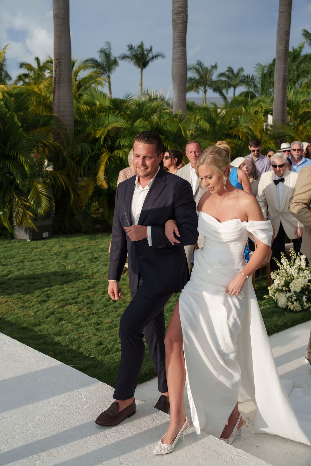 Wedding ceremony processional on white aisle surrounded by tropical palm trees.