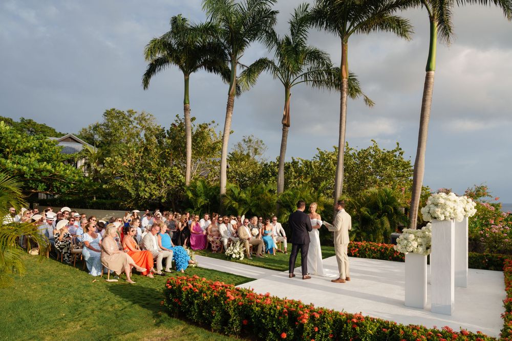 An outdoor wedding ceremony setup with rows of chairs and palm trees under a cloudy sky.