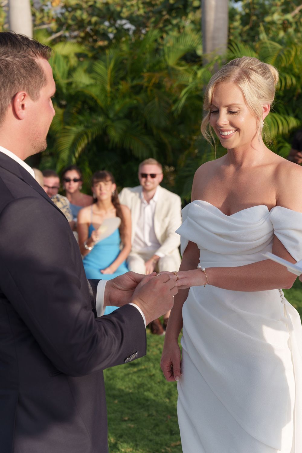 Close-up sequence of a couple exchanging wedding rings during an outdoor ceremony in a tropical garden setting.