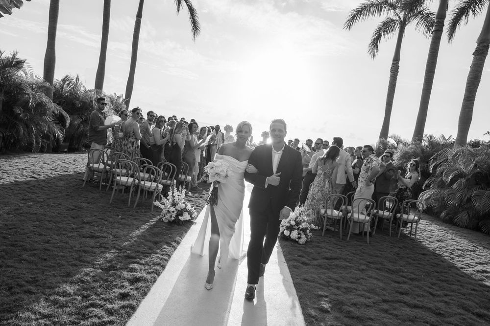 Black and white panoramic collage of an outdoor wedding ceremony setting with palm trees and chairs on a beach.