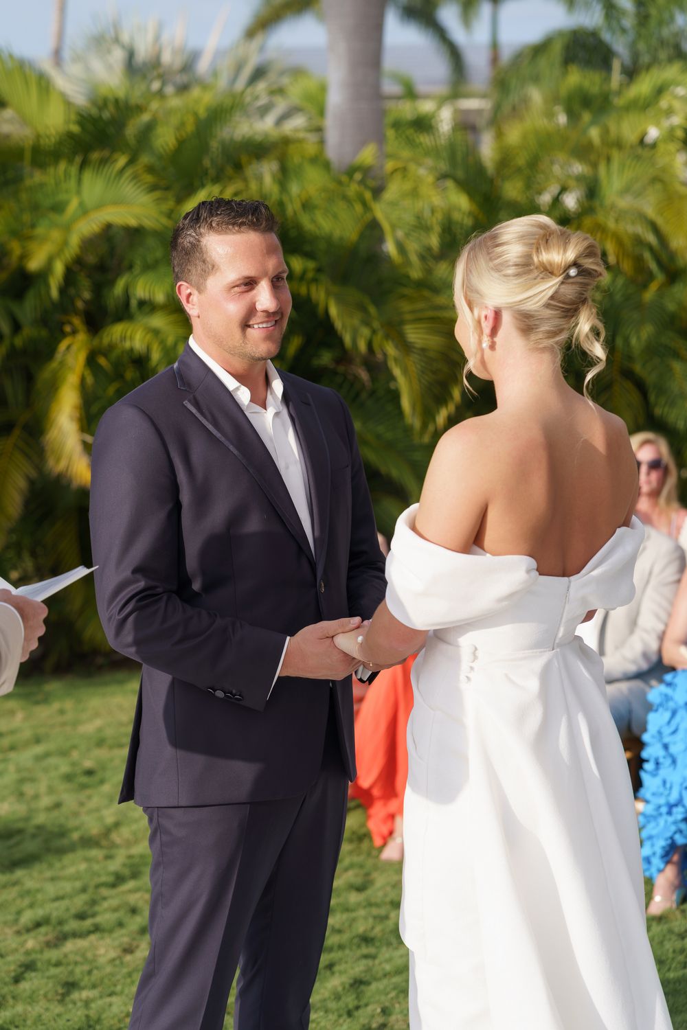 A couple exchanges vows during an outdoor tropical wedding ceremony with palm trees in the background.