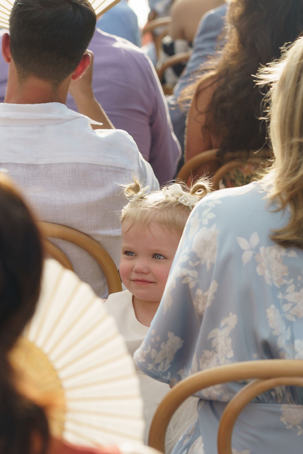 Young guests watch intently during an outdoor event from their seats among the crowd.