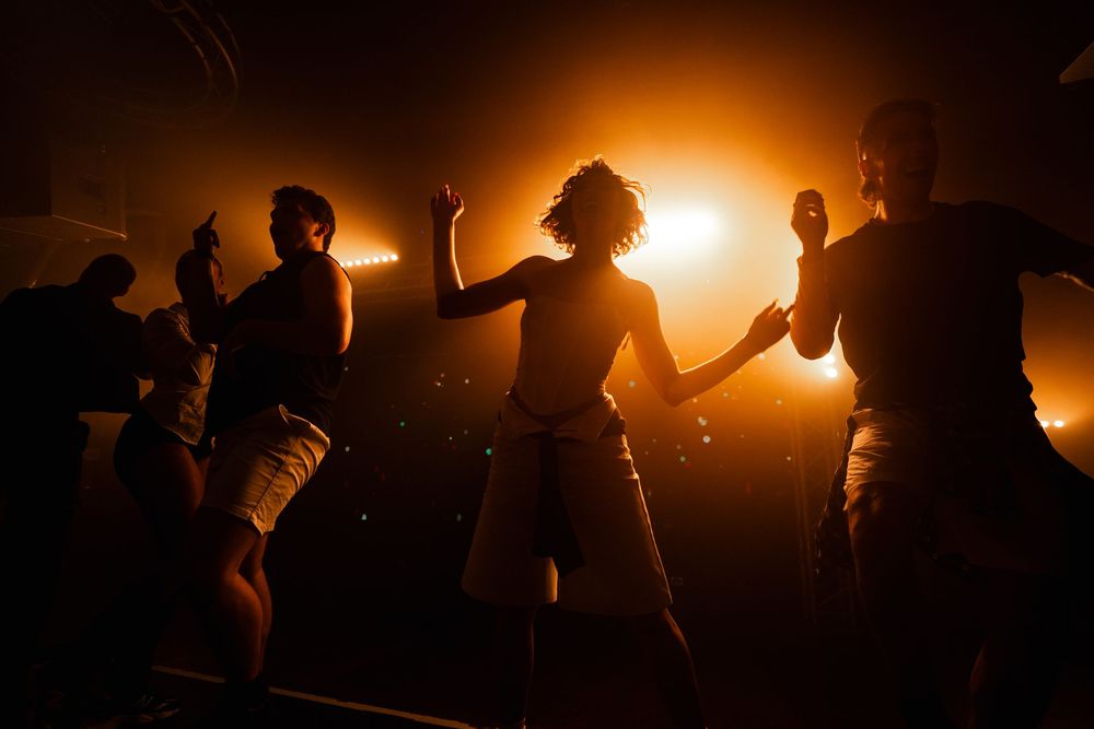 Silhouetted figures dancing energetically against a warm glowing sunset background.