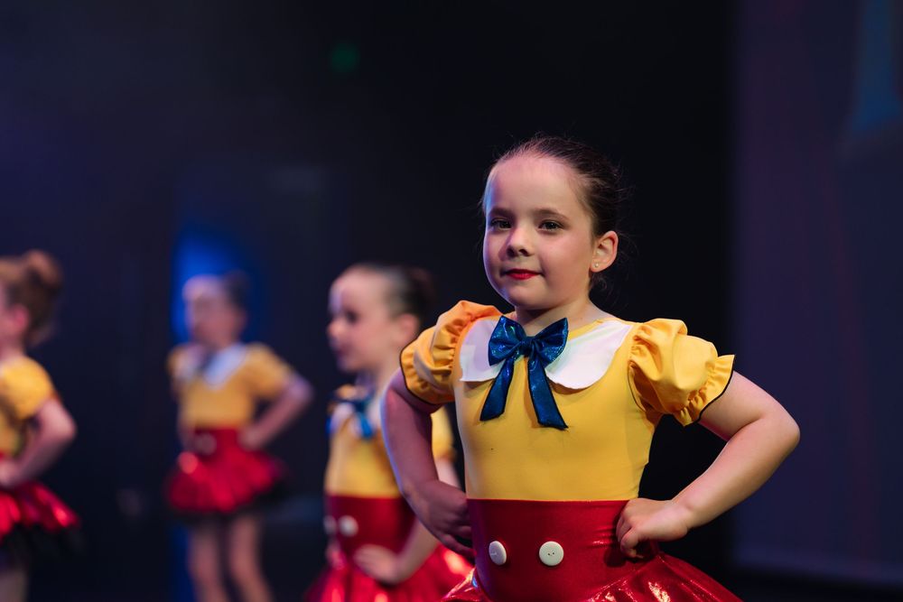 A dancer in a yellow top and red skirt performs on stage during a theatrical production.