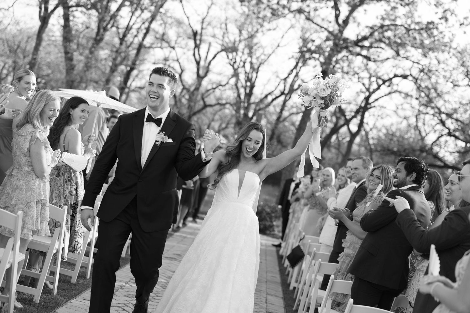 Joyful couple celebrates while walking down the aisle at an outdoor wedding ceremony surrounded by guests.