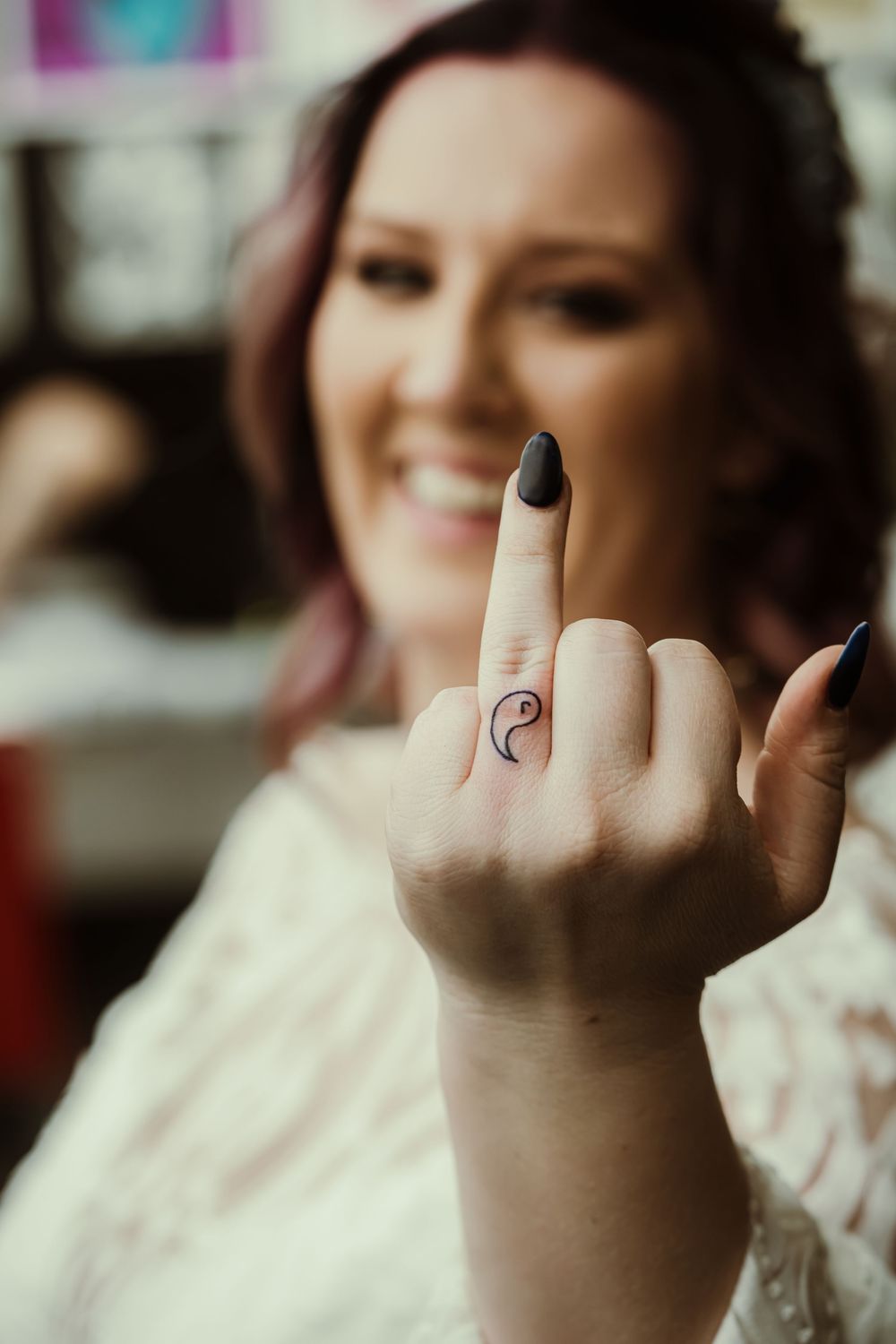 A hand shows off a small tattoo of a yin yang symbol on the finger with a blurred background.