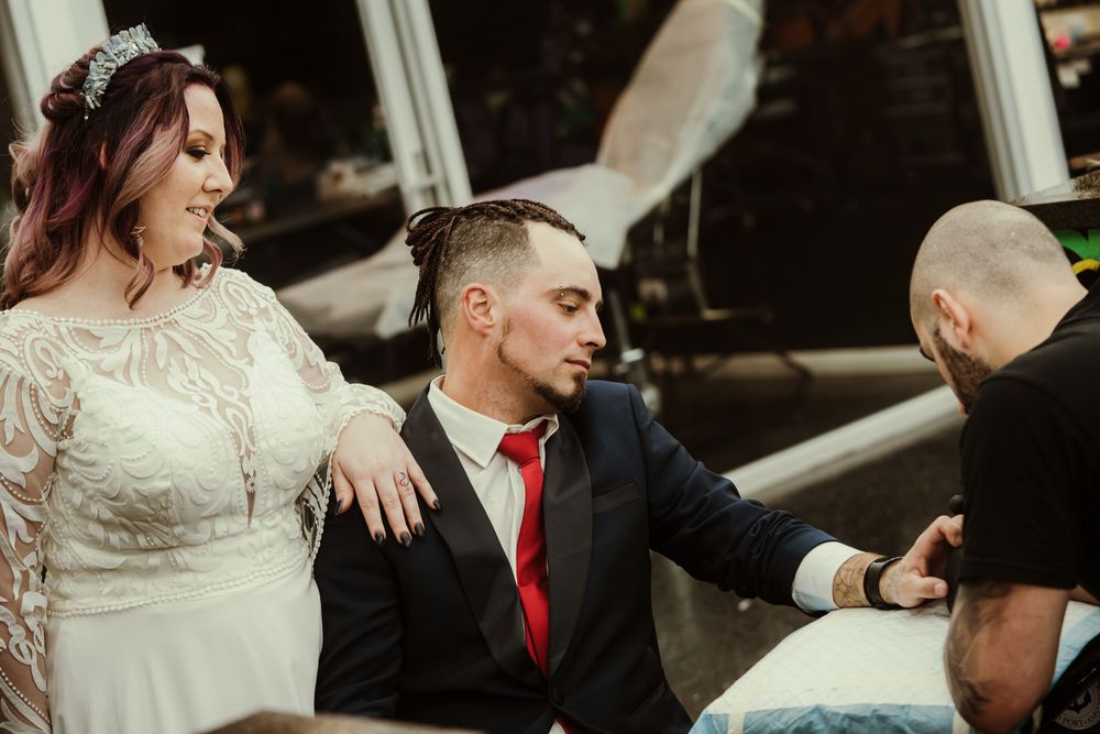 A bride and groom share an intimate moment at their wedding reception while guests socialize in the background.