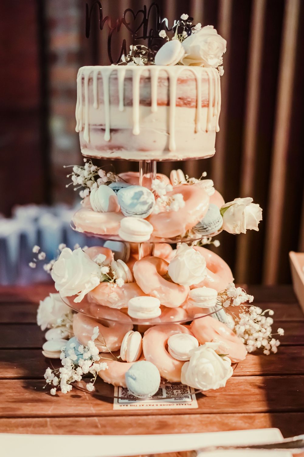 A tiered wedding dessert display with a drip cake on top and pink and blue macarons decorated with baby's breath flowers.