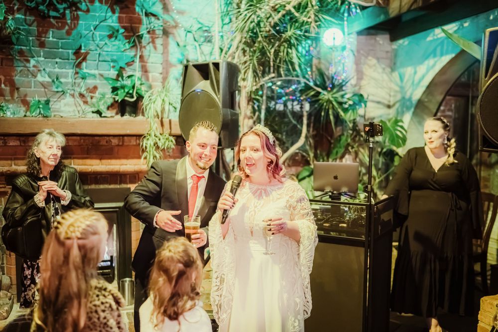 Wedding party dancing and celebrating under teal and green lighting at a reception venue.