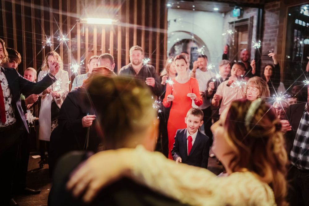 Wedding guests hold sparklers creating magical lighting effects during an evening celebration.