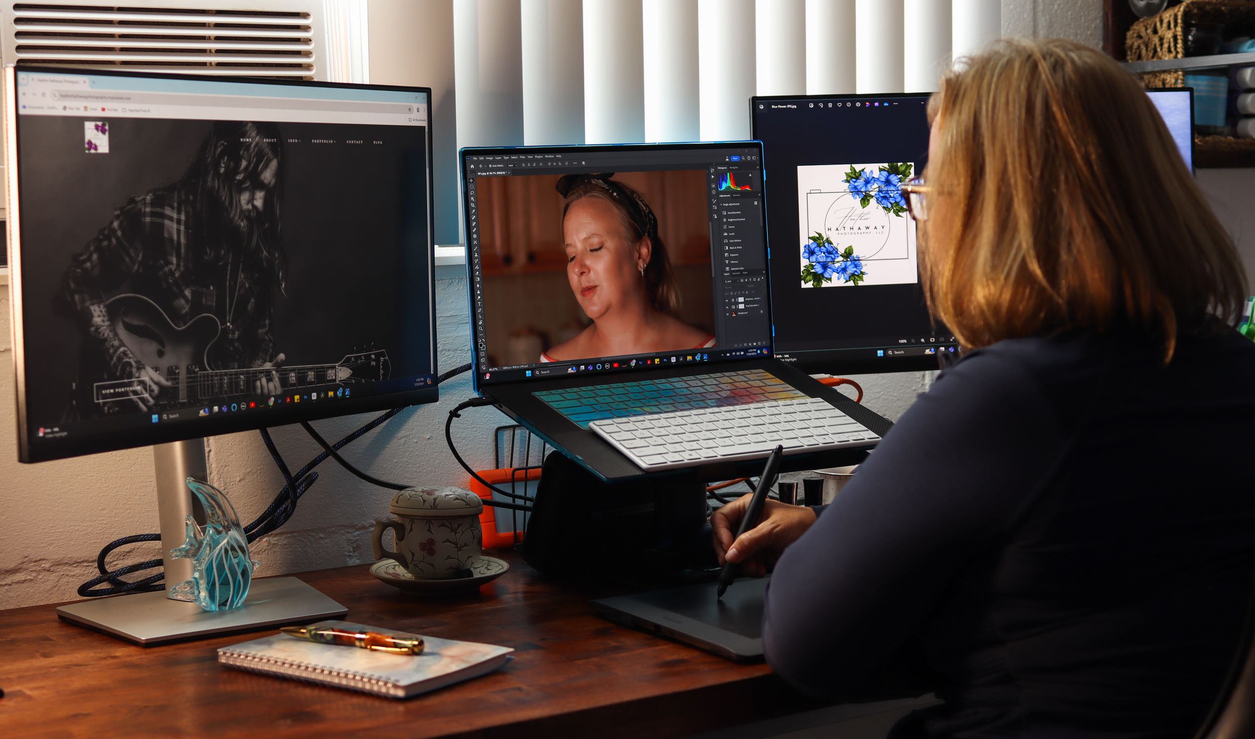 Digital artist working at desk setup with multiple screens showing portrait and black and white artwork.