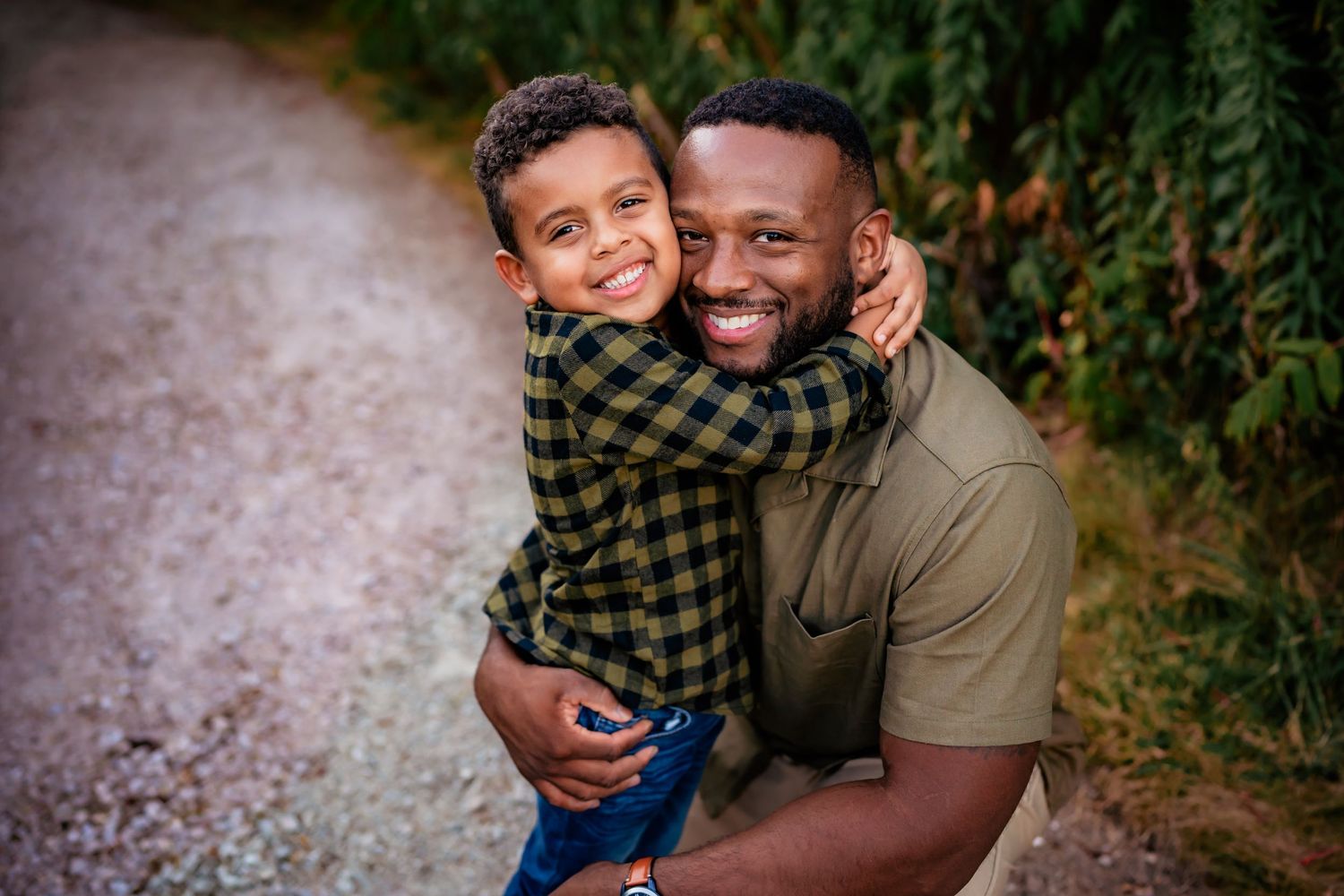 A heartwarming outdoor portrait of a loving parent and child embracing and smiling on a gravel path.