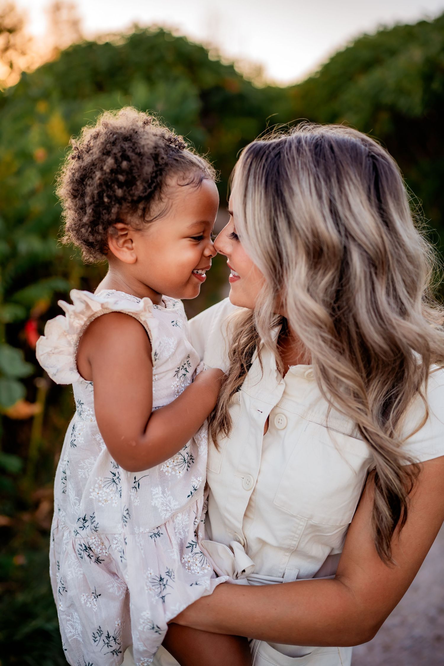 A touching moment of joyful laughter and connection between parent and child wearing white dresses outdoors at sunset.