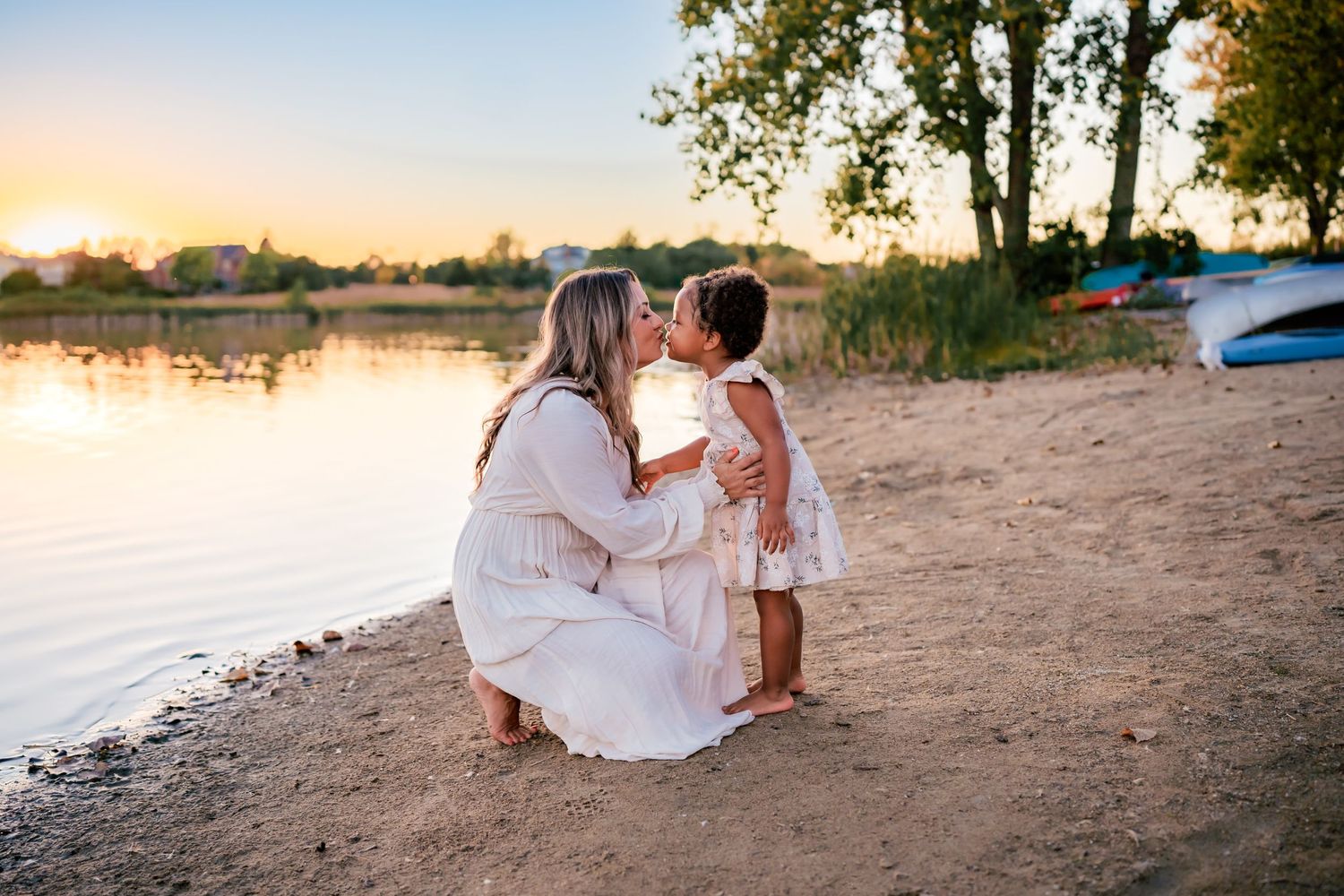 A tender moment shared between two people on a sandy beach at sunset with a tranquil lake in the background.