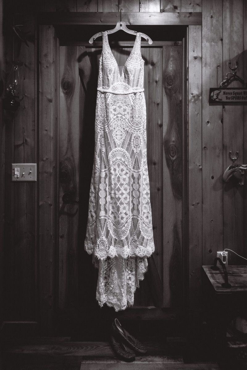 A black and white photo of a lace wedding gown hangs on the door of a barn at a DIY wedding event.