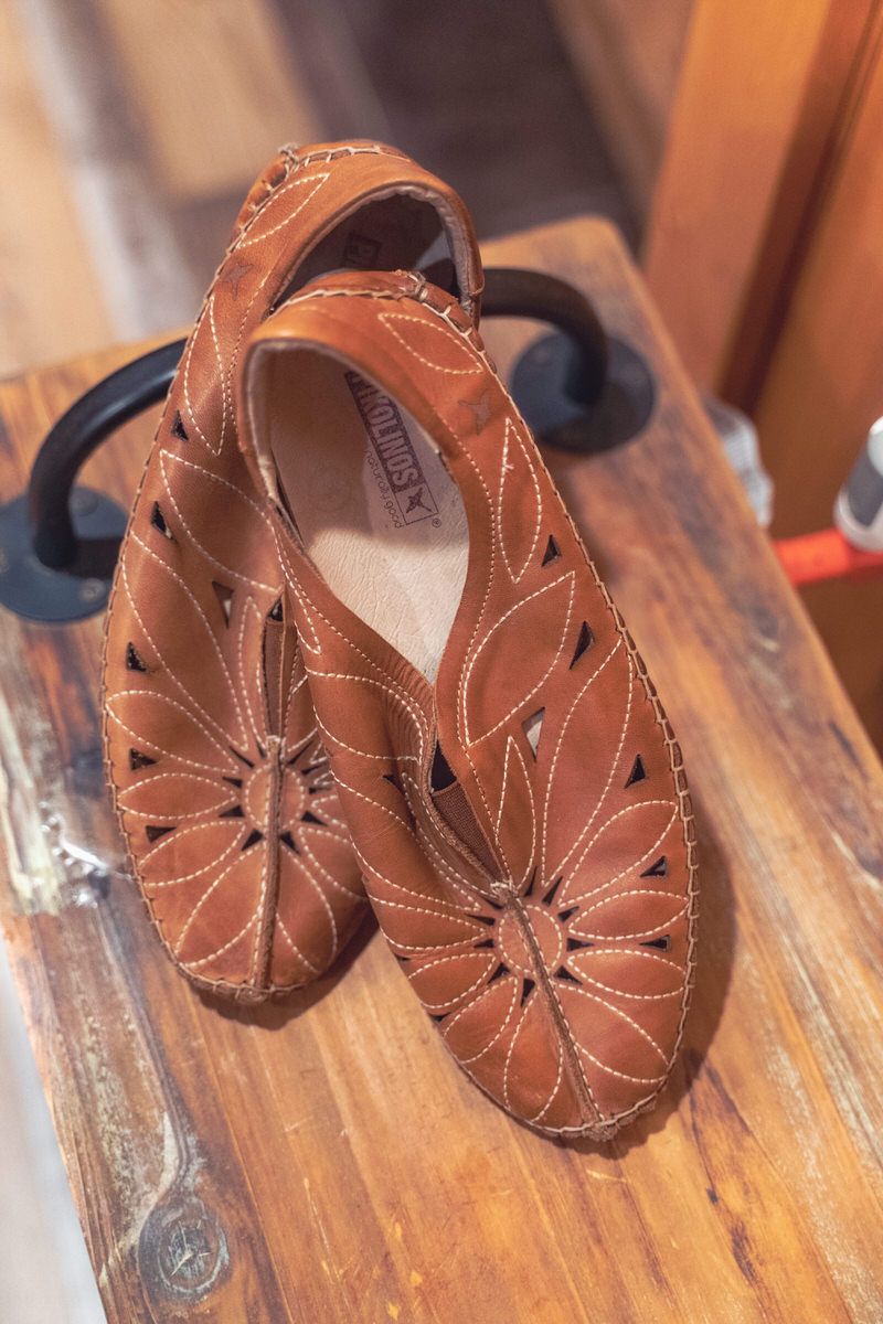 Leather wedding shoes are casually placed on a bench in a barn for a DIY backyard wedding.