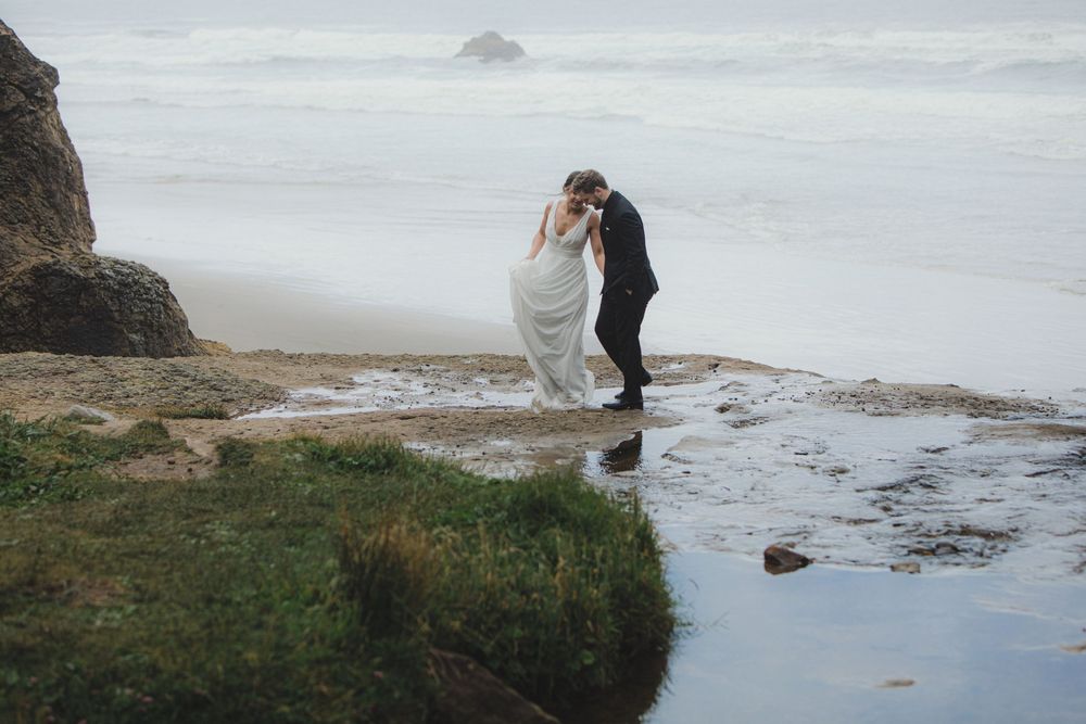 Two figures embrace on a misty coastal cliff edge near crashing waves and rocky shore at dusk.