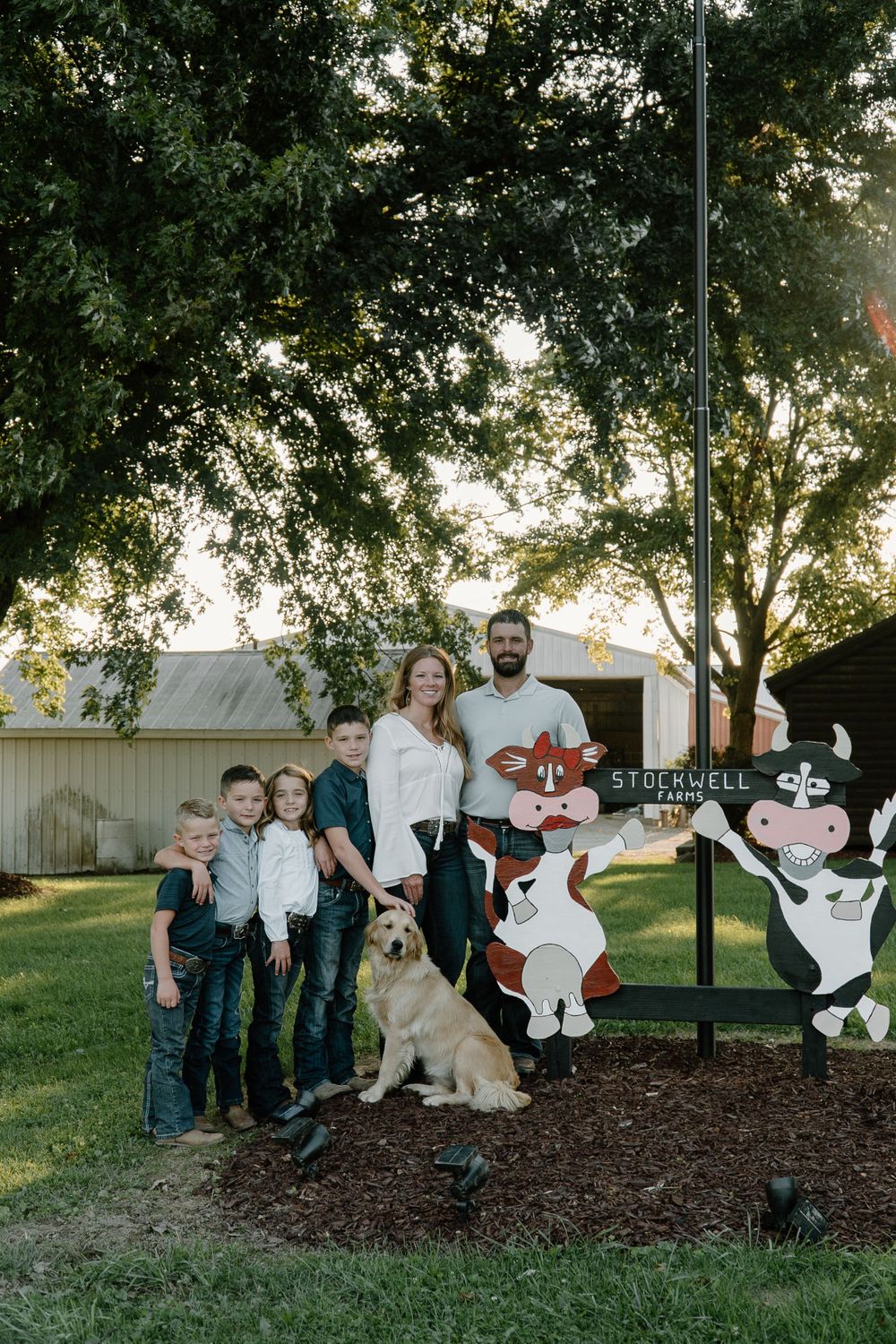 A group poses with their dog in front of decorative cow cutouts in a backyard setting.
