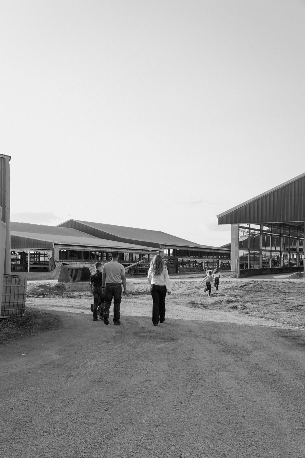 People walking on a path between dairy farm buildings on a sunny day.
