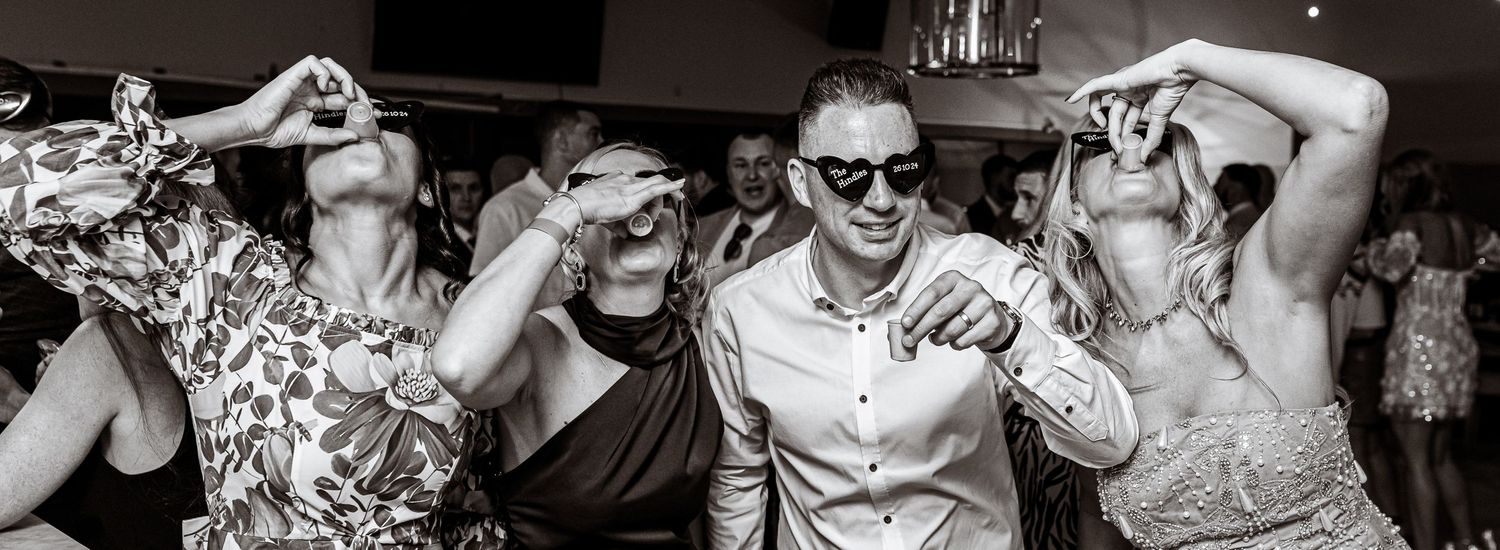 Black and white panoramic shot of people dancing and celebrating at a party.