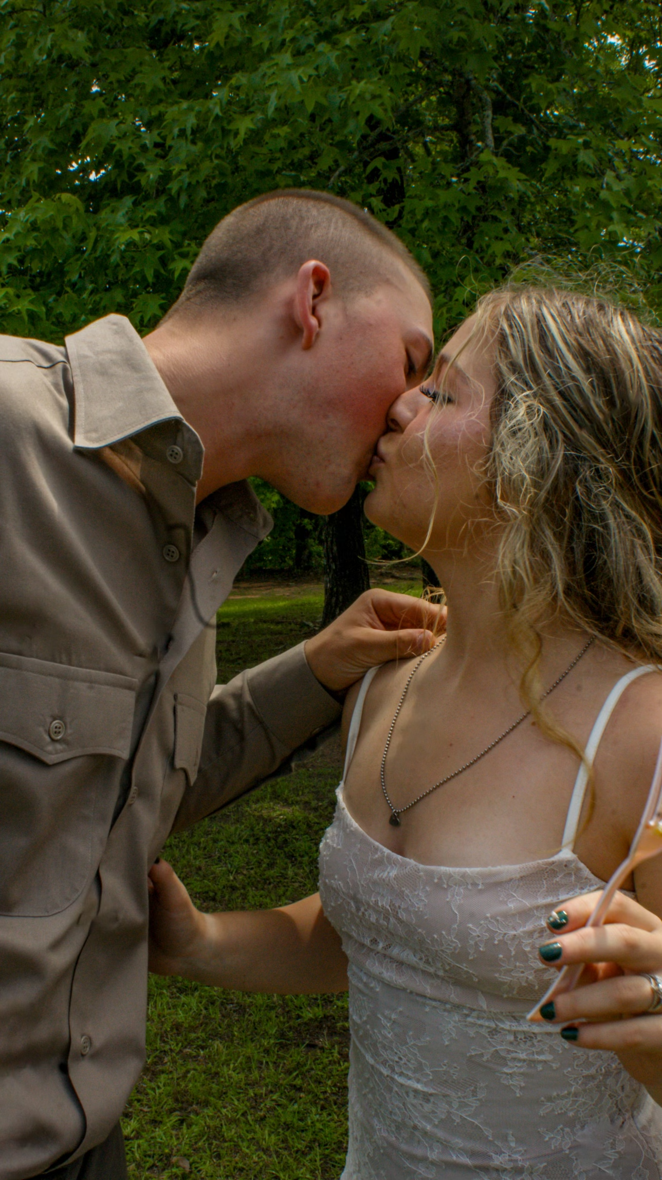 A romantic wedding couple shares a tender kiss outdoors surrounded by lush greenery.