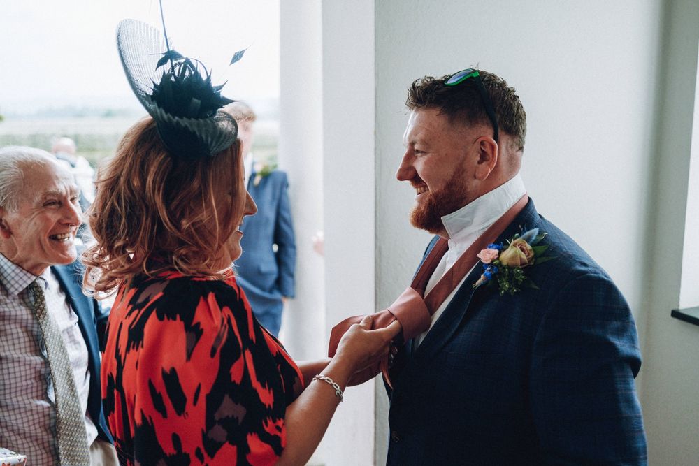 A person in blue suit laughs while someone in red adjusts their boutonniere at a formal event.