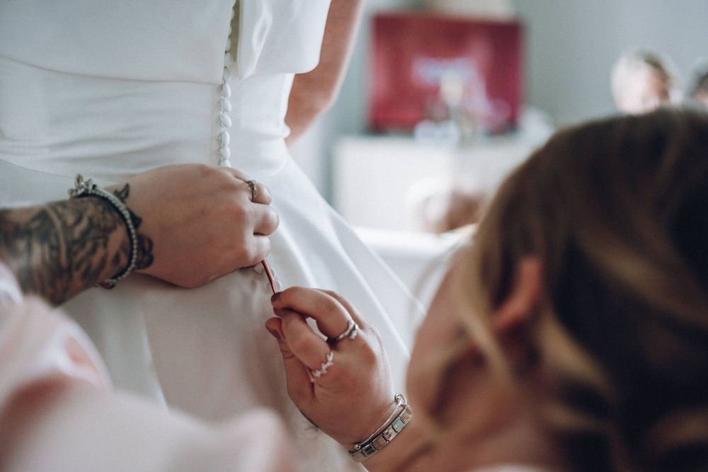 A person wearing a white garment gets help with buttons or fasteners from someone with jewelry and bracelets.